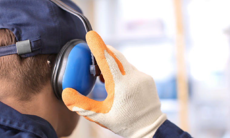 A man wears blue noise reducing headphones while working in a factory.
